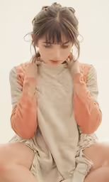young girl wearing a gray sweater and brown shorts sitting down