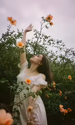 a young woman in white dress reaching up at yellow flowers