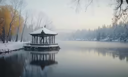 a small building near a lake in the winter