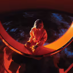 the woman is sitting on the crescent shaped sculpture,a woman sits alone in a large orange tunnel