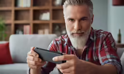 the older man looks at his cellphone while sitting on a couch