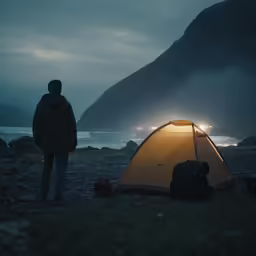 a man standing next to a tent with the lights on in front of him