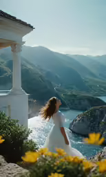 a woman wearing a wedding dress standing on a hill by water