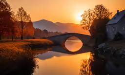 a stone bridge spans the river and a house in the background