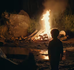 a child looking at a fire in the field at night
