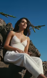 a woman wearing white sits on some rocks