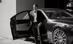 a man in a suit standing in front of a parked car