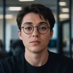 a young man wearing round glasses and staring at the camera