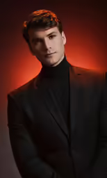 a man in a black suit standing in front of a red light