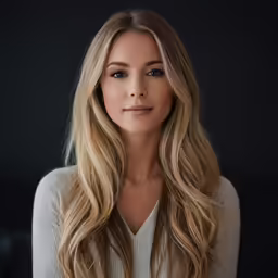 a woman with blonde hair standing by a black wall