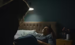 a woman standing next to a man in bed