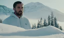 a man stands in the snow with mountains behind him