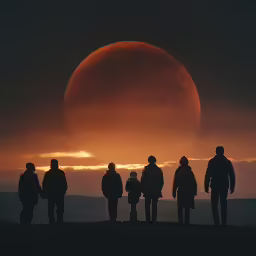 four people watch the solar eclipse as it rises over the mountains