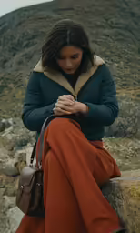 a woman wearing an orange and green coat, black jacket, and bag