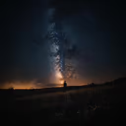 there is a dark sky with stars and a lone man looking at the stars in the sky