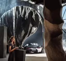 a woman standing in front of a car next to a tall arch