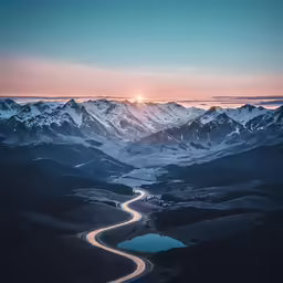 the sun sets over the mountains and the road passes by