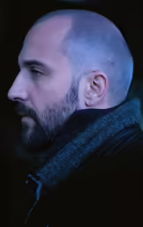 a bald man in jacket staring ahead at something