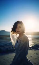 woman standing on the beach near the ocean with sheer fabric over her face