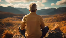 a man sitting on top of a cliff watching the mountains