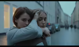 two girls are embracing outside and standing in the street