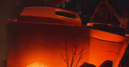 fire lit, shiny and bright in an outdoor room,a glowing pot sits beside a tree and bush