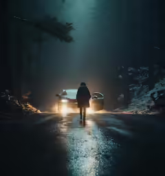 a person walking down a road near a car at night