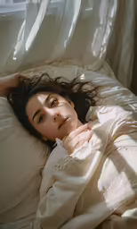 a woman is laying in bed looking off into the distance