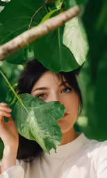 a woman is looking over the leaves of a plant