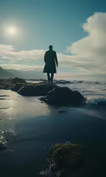 a person on rocks in the ocean with a blue sky and sun in the background