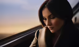 woman on train looking out window and holding her head