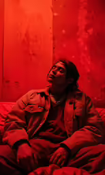 a person sits on a bed against a red wall