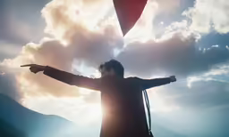 a man with arms outstretched, facing the sky, with a kite in his hand
